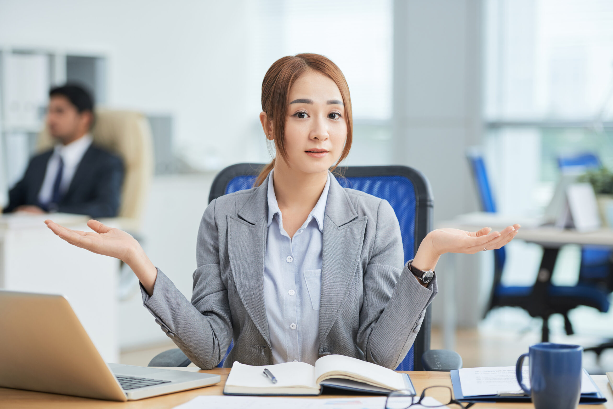 asian-woman-sitting-desk-office-looking-camera-with-helpless-hand-gesture